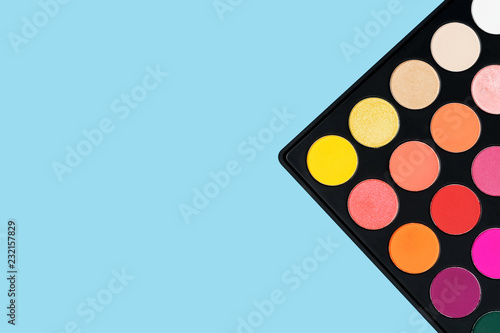 Black plastic palette of brightly coloured yellow, red, pink, orange eyeshadow placed in the corner of pastel baby blue background shot with studio light from above © Anna Anisimova