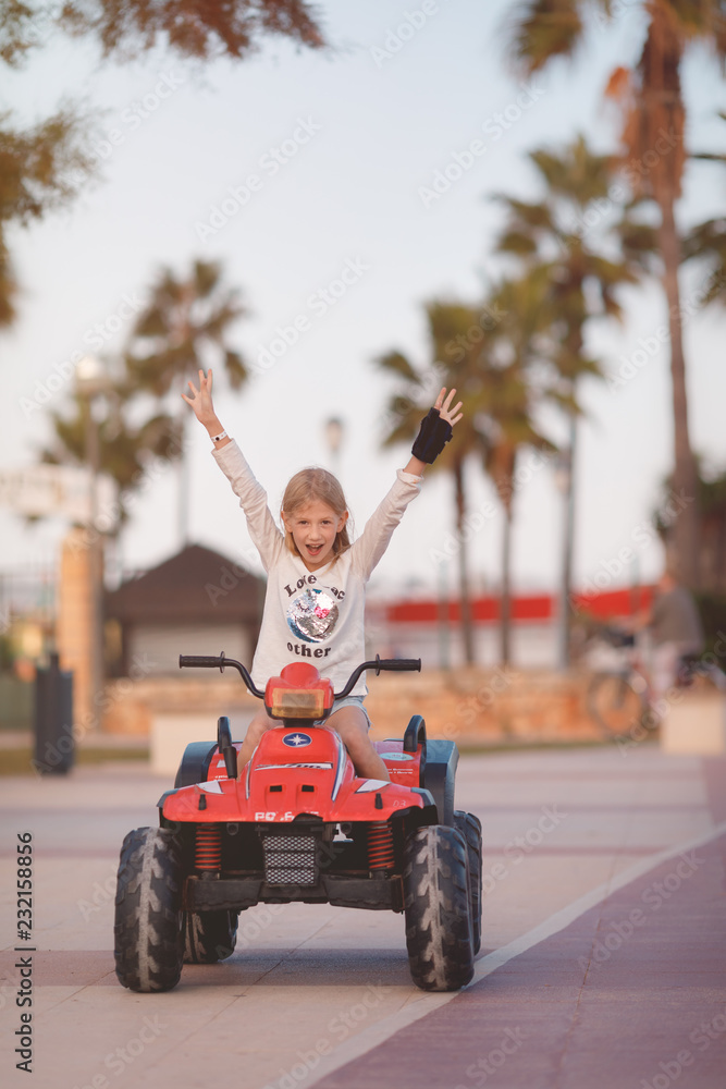 Young blond girl riding in electric toy car, lifting up arms in the air Young blond girl riding in electric toy car, lifting up arms in the air