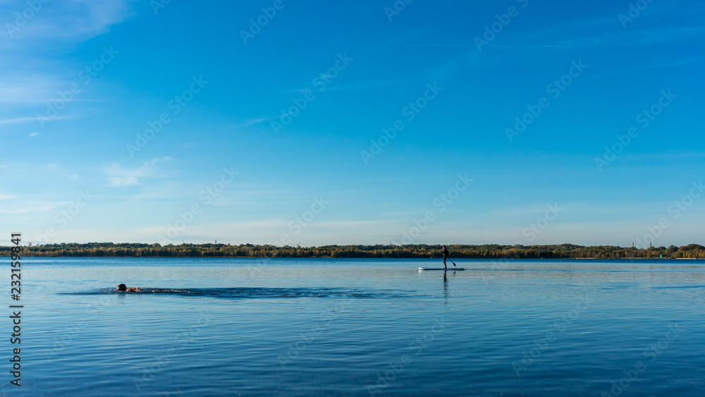 Triathlete swimming in a blue lake, sail boat far away