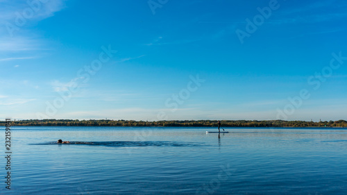 Fototapeta Naklejka Na Ścianę i Meble -  Triathlete swimming in a blue lake, sail boat far away