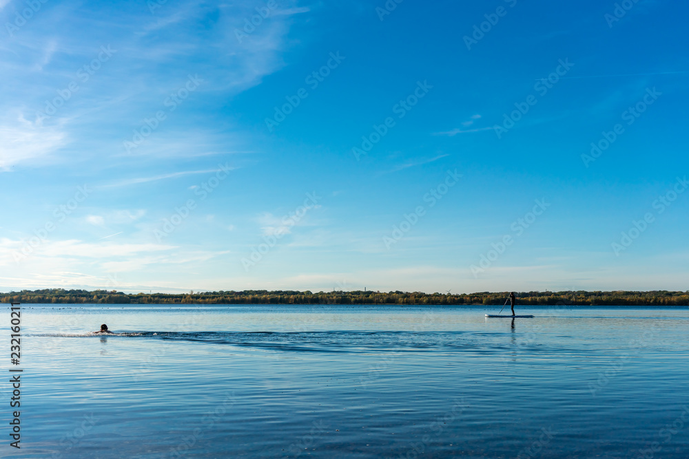Triathlete swimming in a blue lake, sail boat far away