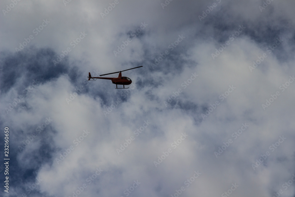 Red helicopter high in the blue sky with white clouds Red helicopter high in the blue sky with white clouds