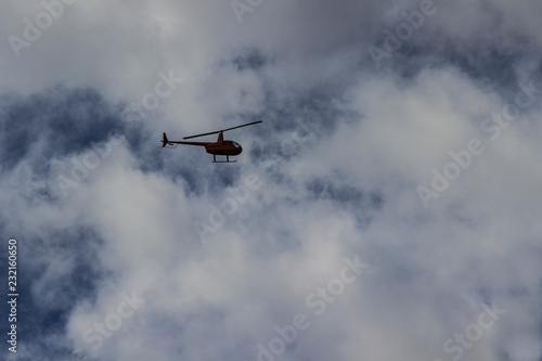 Red helicopter high in the blue sky with white clouds