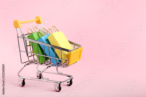 Fotografie, Obraz Small paper shopping bags with shopping cart on pink background