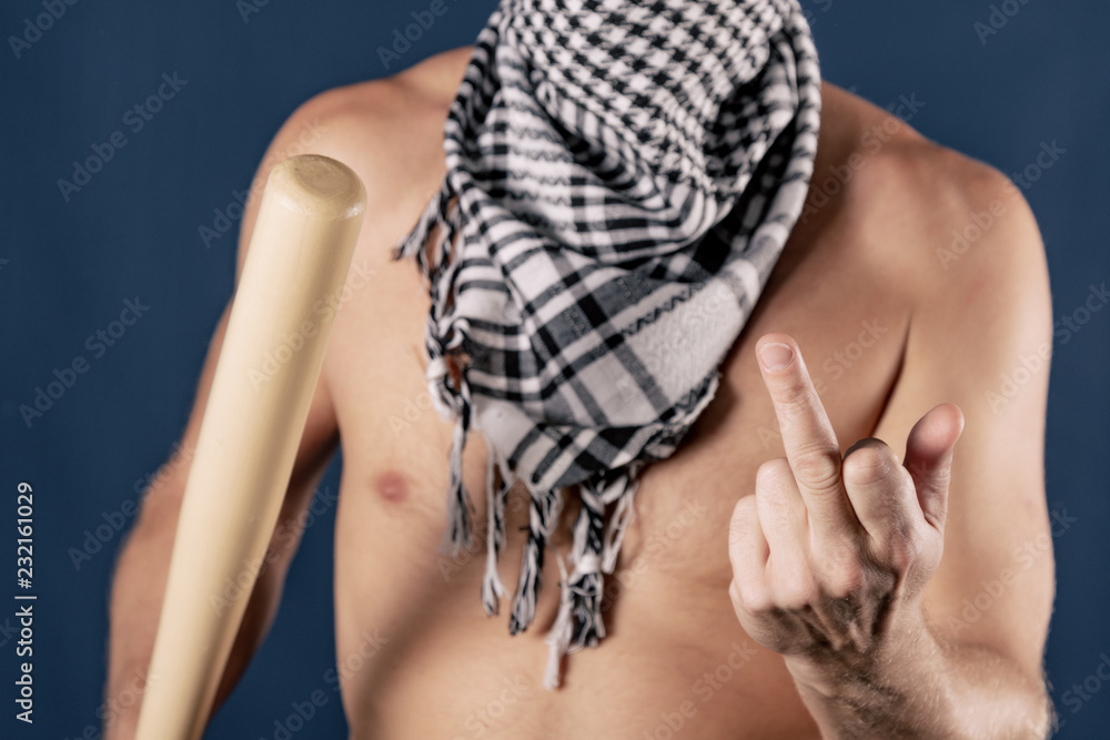 Portrait of a shirtless man in checkered scarf holding a baseball bat and shows finger on blue background