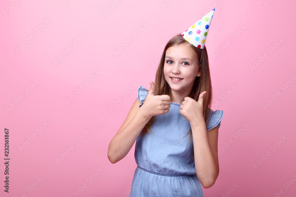 Cute young girl in birthday hat on pink background