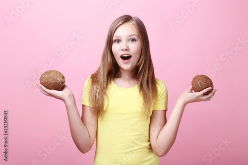 Cute young girl with coconuts on pink background