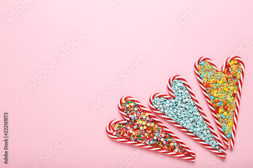 Christmas candy canes in heart shape with colorful sprinkles on pink background