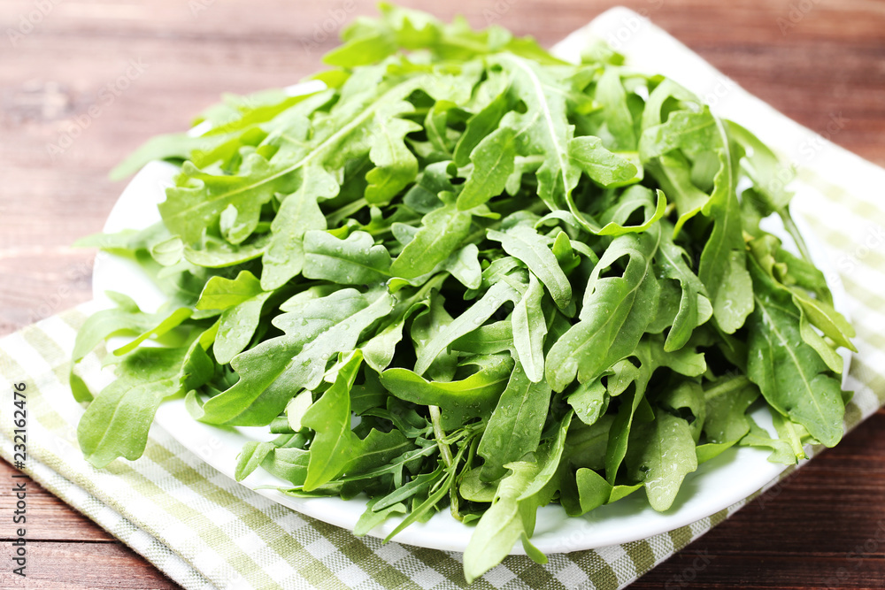 Green arugula leafs in plate with napkin on wooden table Green arugula leafs in plate with napkin on wooden table