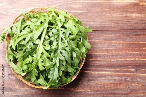 Green arugula leafs in basket on brown wooden table