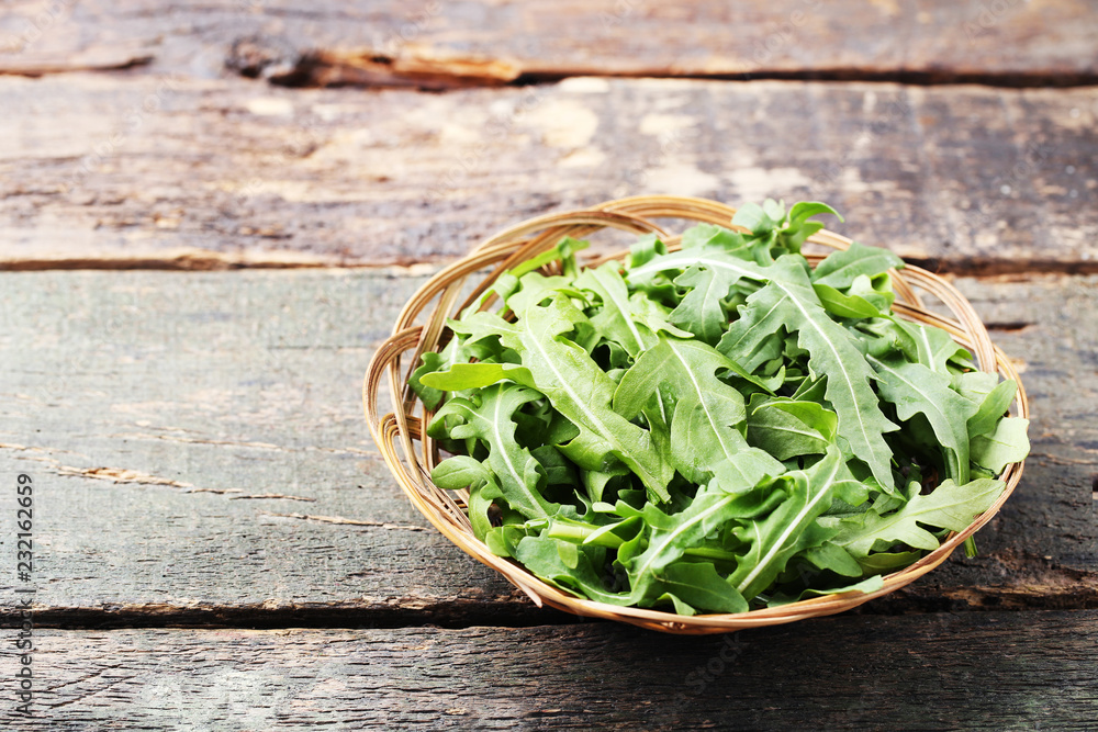 Fototapeta premium Green arugula leafs in basket on wooden table