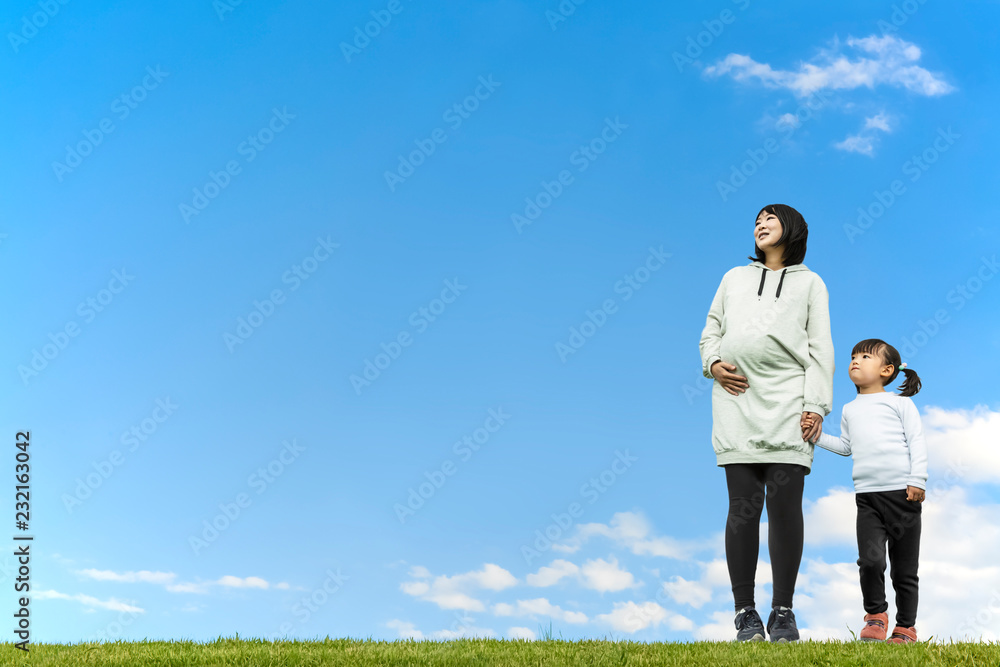 青空を背景に手をつなぎ遠くを見つめる幼い女の子とお母さん。親子、家族、愛、幸せイメージ