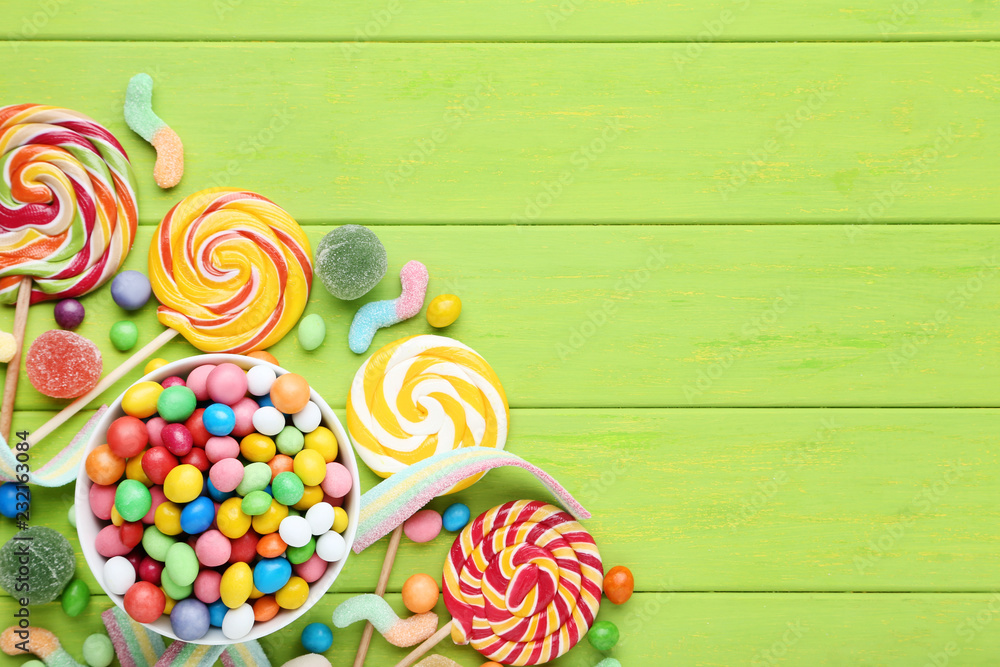 Sweet candies in bowl and lollipops on green wooden table Sweet candies in bowl and lollipops on green wooden table