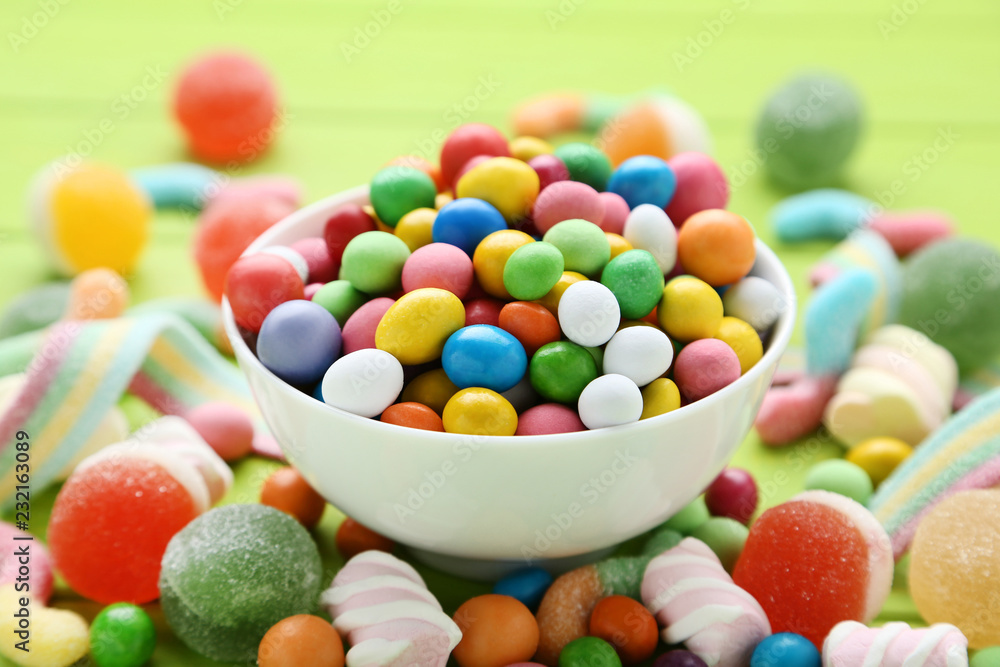 Colorful sweet candies in bowl on green background Colorful sweet candies in bowl on green background