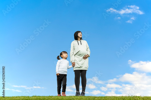 青空を背景に手をつなぎ遠くを見つめる幼い女の子とお母さん。親子、家族、愛、幸せイメージ © chikala