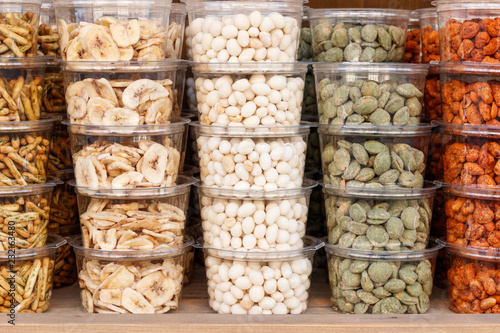 Stacked transparent plastic trays full of different kinds of nuts on the shelf of a store full of delicacies.