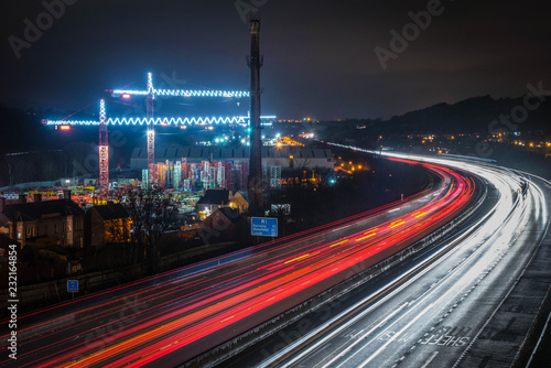 Lights From Heavy Traffic On The M1 Motorway As They Snake Past Two Illuminated Cranes