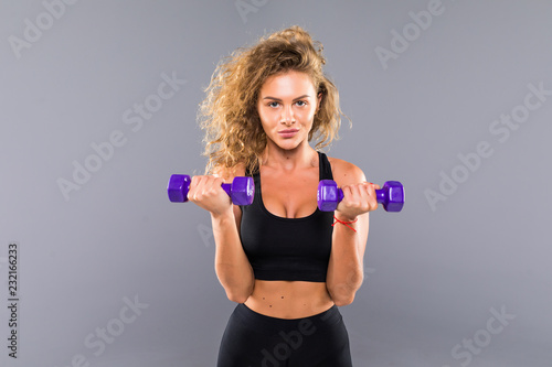 Portrait of pretty curly sporty girl holding weights dumbbels isolated on gray background