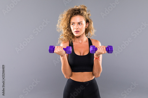 Portrait of slim sporty woman doing exercises with small dumbbells isolated over gray background