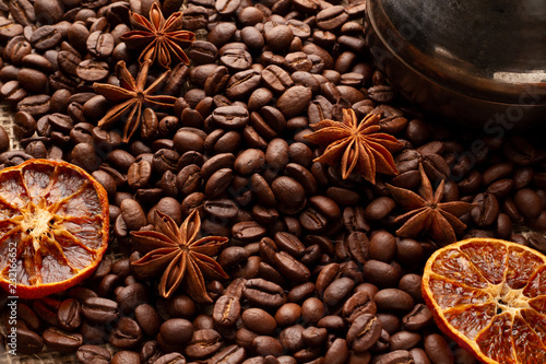 A table covered with coffee beans with cinnamon, anise stars and dried orange. Cover or background for a coffee menu. With coffee brew for brewing. High angle of a photo on coffee subject.