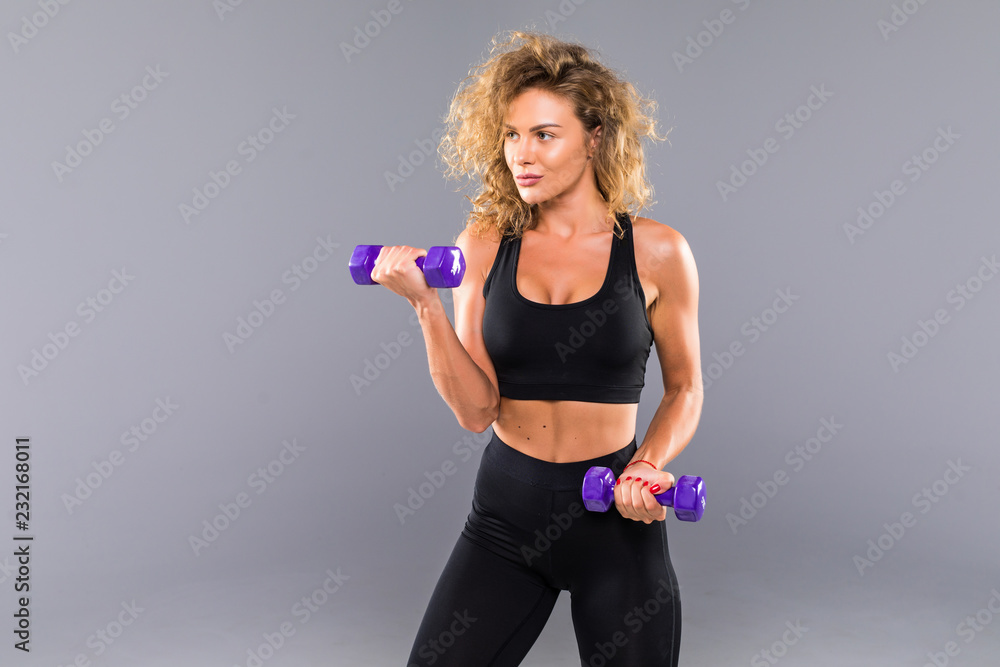 Attractive brunette sporty woman in black sportswear holds dumbbells isolated on gray background. Attractive brunette sporty woman in black sportswear holds dumbbells isolated on gray background.