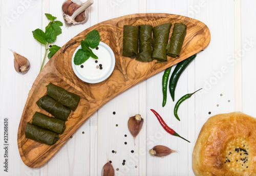 Dolma on wooden plate with hot peppers, garlic, mint and sour cream on white background top view photo