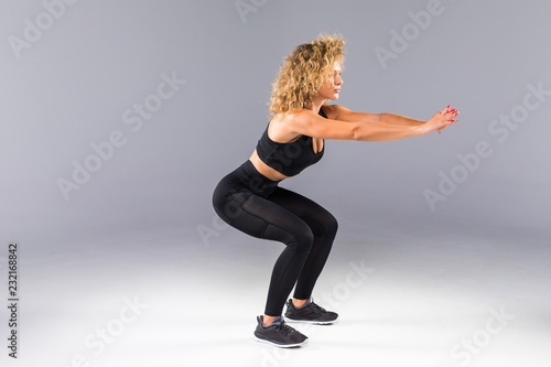 Portrait of sporty athletic woman in sneakers and tracksuit squatting doing sit-ups in gym isolated over gray background © F8  \ Suport Ukraine