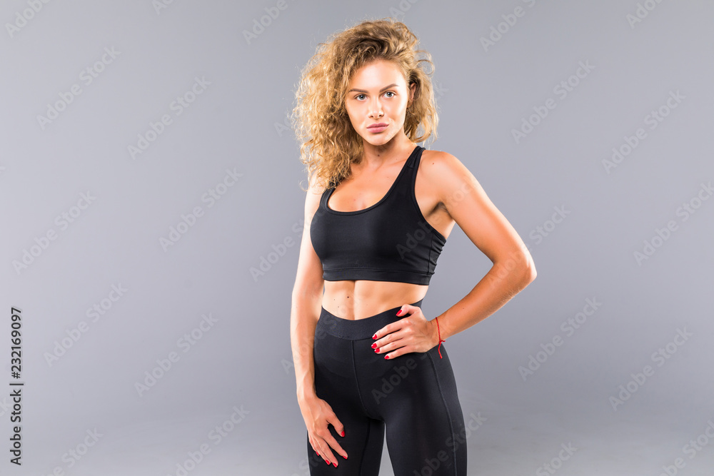 Portrait of sexy young woman with her hands on hips looking at camera. Fitness female with muscular body ready for workout on grey background Portrait of sexy young woman with her hands on hips looking at camera. Fitness female with muscular body ready for workout on grey background
