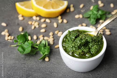 Homemade basil pesto sauce in bowl and ingredients on table