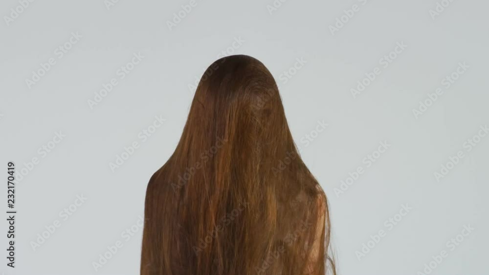 Slow motion shot of a woman letting her very long brown hair go over her head. 