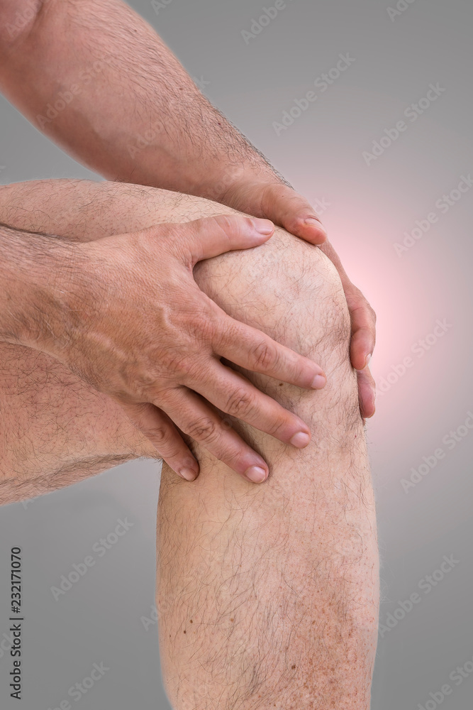 Fototapeta premium Man suffering from knee pain.A mature man massaging his painful knee, suffering from painful knee joint on grey from frofile