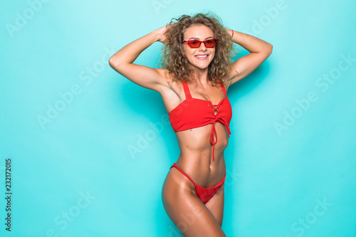 Beautiful young curly woman in a sunglasses and red swimsuit on a green background © F8  \ Suport Ukraine