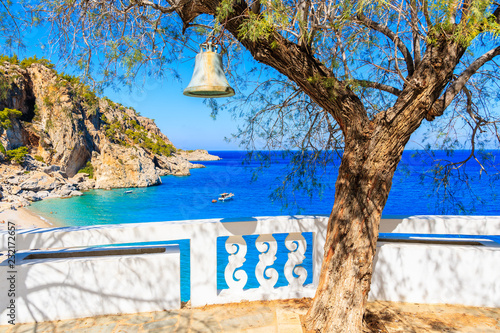 Bell hanging on tree and view of Kyra Pynagia beach from church terrace on Karpathos island, Greece photo