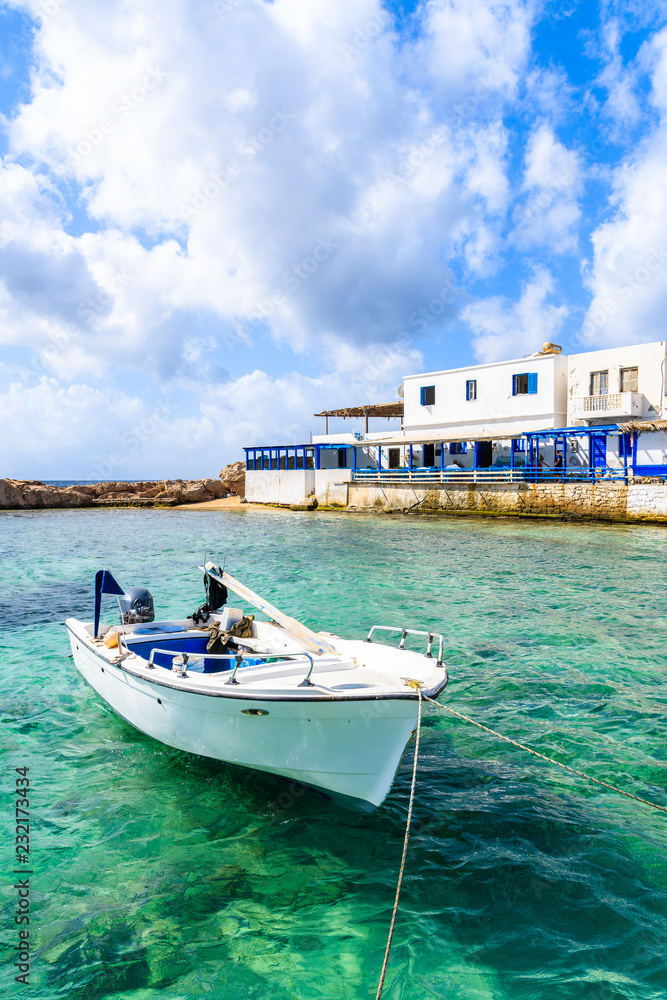 White fishing boat on sea in Lefkos port with typical houses on shore, Karpathos island, Greece