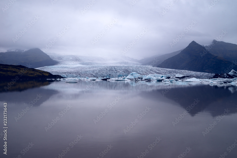 A moody photo of a glacier reaching down to the lake at its feet. 