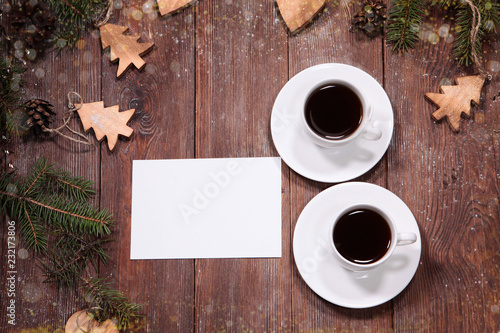 Branches of the Christmas tree, decorated with toys for New year or Christmas. Wooden background. Two cups of coffee and a piece of paper for any inscription. The label for the label.