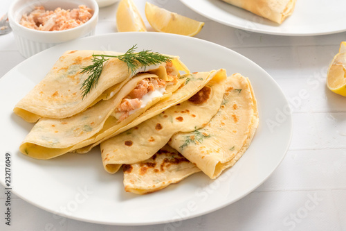 Crepes filled with dill, cream cheese and smoked salmon on white plate.