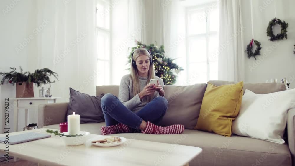 A young woman with headphones and smartphone at home at Christmas time. A young woman with headphones and smartphone at home at Christmas time.