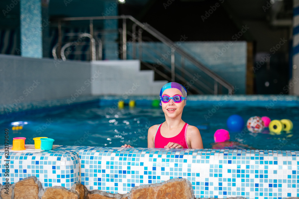 Happy girl with swimming hat and glasses in the blue pool indoor