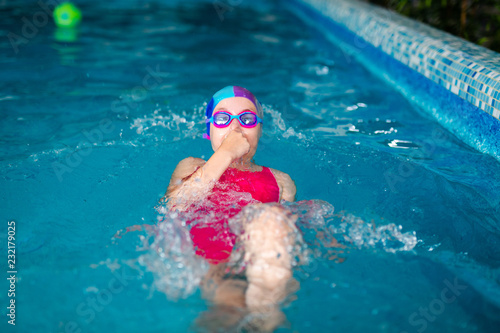 Happy girl with swimming hat and glasses in the blue pool indoor photo