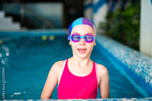 Happy girl with swimming hat and glasses in the blue pool indoor photo