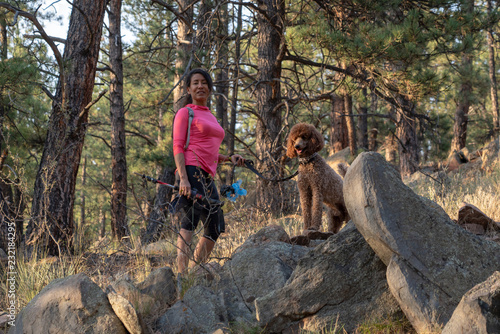 A hispanic woman is hiking with a dog, at sunset, in the Rocky Mountains near Denver, Colorado, USA