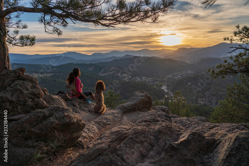 A hispanic woman is hiking with a dog, at sunset, in the Rocky Mountains near Denver, Colorado, USA