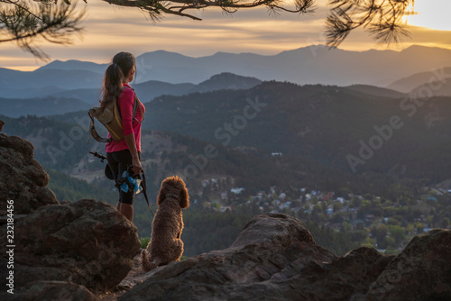 A hispanic woman is hiking with a dog, at sunset, in the Rocky Mountains near Denver, Colorado, USA