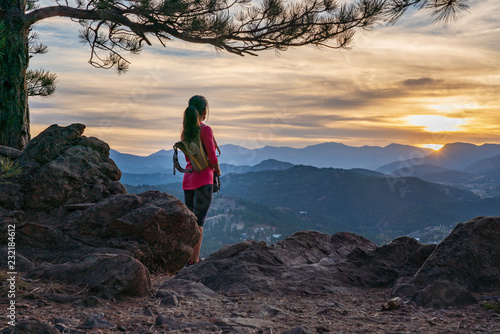 A hispanic woman is hiking with a dog, at sunset, in the Rocky Mountains near Denver, Colorado, USA