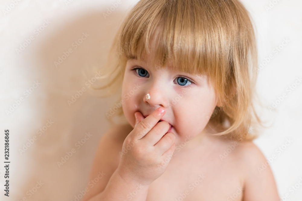 Little blonde baby girl two years old in pink pants sitting on the white table near her birthday cake and different pink sweets on the table Little blonde baby girl two years old in pink pants sitting on the white table near her birthday cake and different pink sweets on the table
