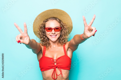 Portrait of amazing young woman showing peace gesture in red bikini isolated over green background.