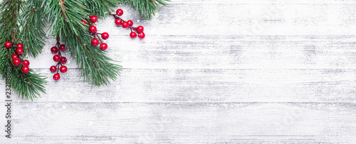 Christmas background with tree branches and holly berries. White wooden table. Snowfall drawing effect. Top view. Copy space