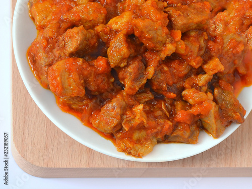Homemade food: meat stewed with carrots, onions and paprika on a white plate close up