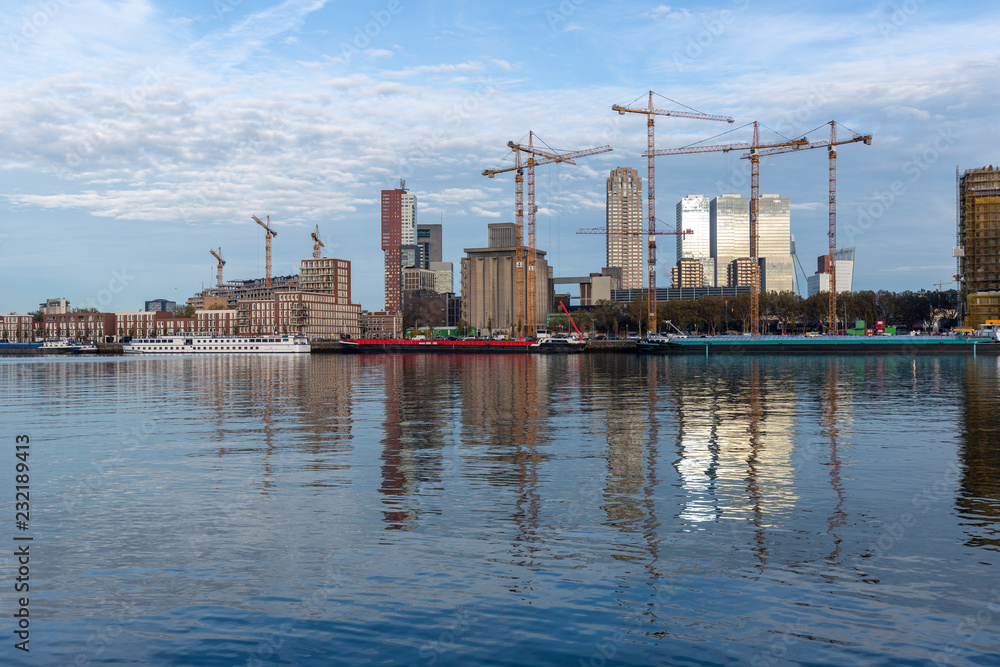 Urban view with modern buildings inhabited by cranes in the Dutch city of Rotterdam with a reflection in the river